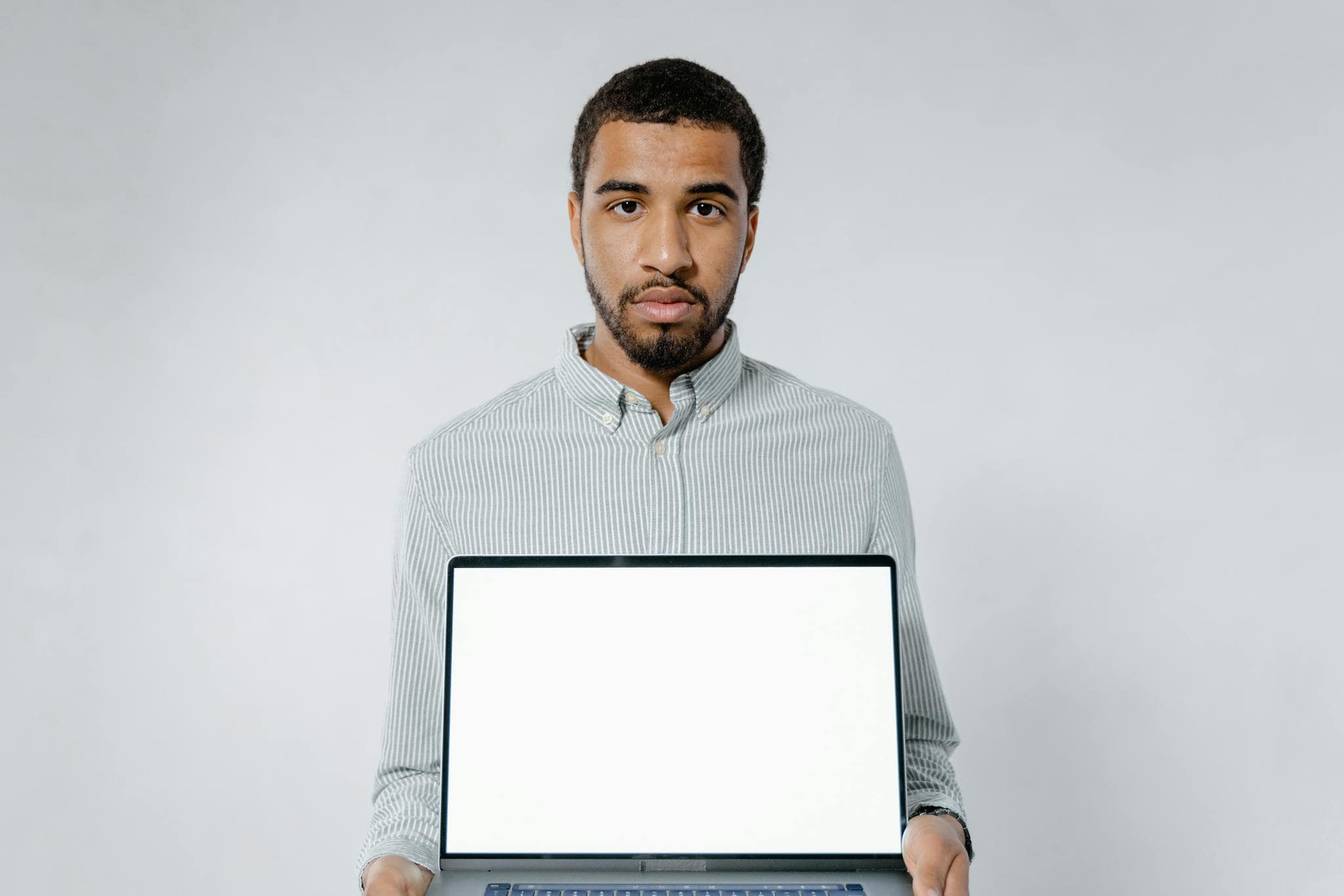 Adult man presenting a laptop with a blank screen, ideal for mockups or design work.